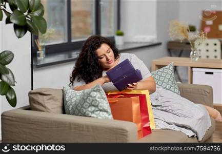 consumerism, people and sale concept - young woman with shopping bags and wallet sitting on sofa at home. woman with shopping bags and wallet at home