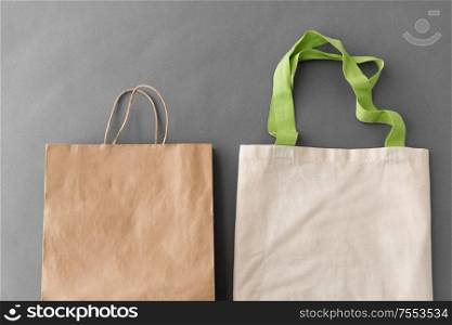 consumerism, recycling and eco friendly concept - reusable canvas tote for food shopping and paper bag on grey background. paper bag and reusable tote for food shopping