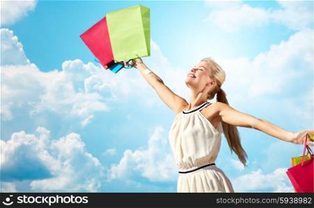 consumerism, sale and people concept - smiling woman with shopping bag rising hands over blue sky and clouds background