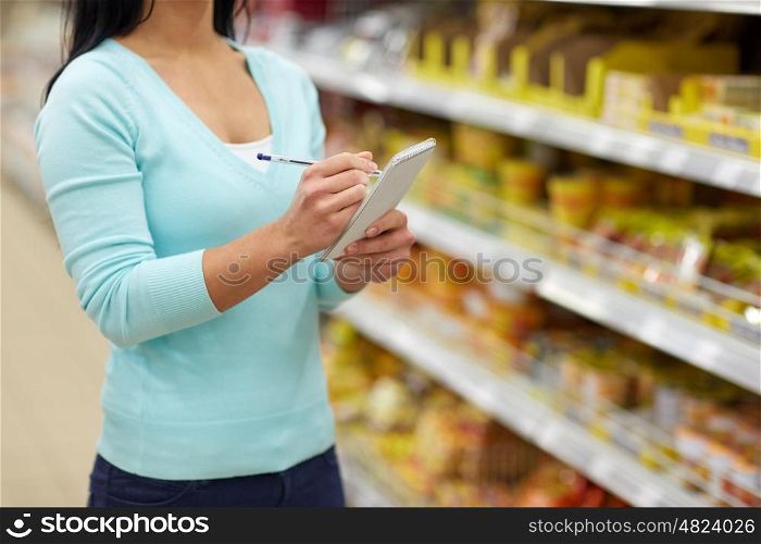 consumerism, shopping and people concept - woman with notebook at grocery store or supermarket