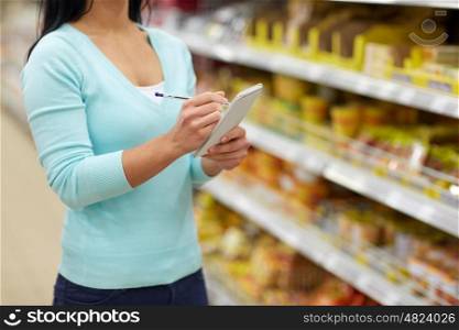 consumerism, shopping and people concept - woman with notebook at grocery store or supermarket