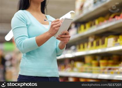 consumerism, shopping and people concept - woman with notebook at grocery store or supermarket. woman with notebook shopping at supermarket
