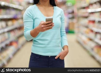 consumerism, shopping, technology and people concept - close up of woman with smartphone at shop or supermarket
