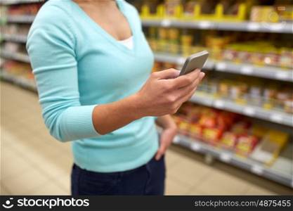 consumerism, shopping, technology and people concept - close up of woman with smartphone at shop or supermarket