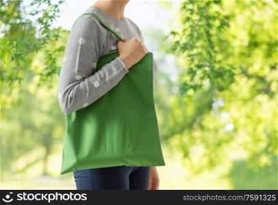 consumerism, sustainability and eco friendly concept - woman with green reusable canvas bag for food shopping over natural background. woman with reusable canvas bag for food shopping