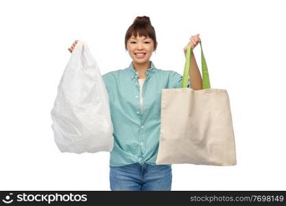 consumerism, sustainability and eco living concept - happy smiling young asian woman in turquoise shirt and jeans with plastic and green reusable canvas bag for food shopping over white background. woman with plastic and reusable shopping bag