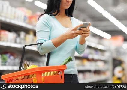 consumerism, technology and people concept - woman with smartphone and shopping basket buying food at grocery store or supermarket. woman with smartphone buying food at supermarket. woman with smartphone buying food at supermarket