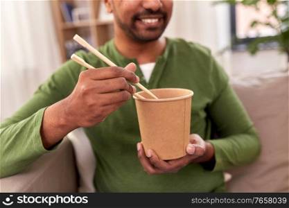 consumption and people concept - smiling indian man eating takeaway food at home. smiling indian man eating takeaway food at home