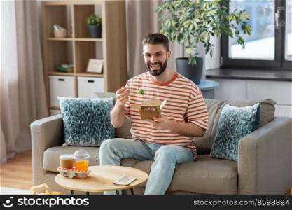 consumption, delivery and people concept - smiling man with fork eating takeaway food at home. smiling man eating takeaway food at home
