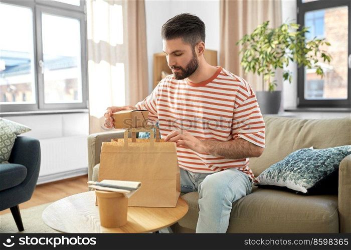 consumption, eating and people concept - man unpacking takeaway food in paper bag at home. man unpacking takeaway food at home