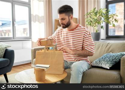 consumption, eating and people concept - man unpacking takeaway food in paper bag at home. man unpacking takeaway food at home