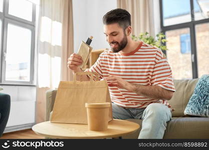 consumption, eating and people concept - smiling man unpacking takeaway food in paper bag at home. smiling man unpacking takeaway food at home