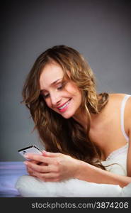 Contact idea. Attractive woman holding smartphone and lying on bed. Gray background.