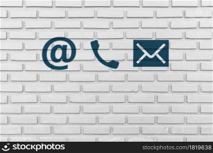 Contact Us. Phone, email and post icons paint on white brick wall