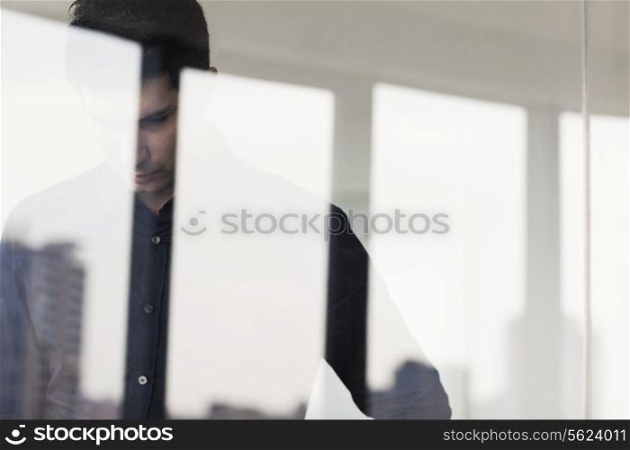 Contemplative businessman looking down on the other side of a glass wall