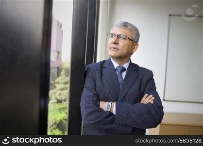 Contemplative mature businessman looking through window at workplace