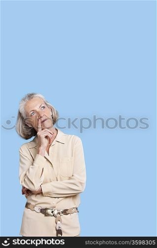 Contemplative senior woman in casuals with hand on chin against blue background