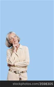 Contemplative senior woman in casuals with hand on chin against blue background