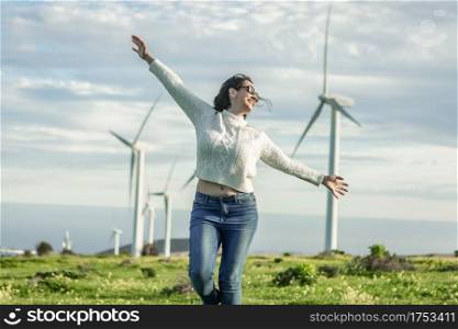 Content female standing with outstretched arms in meadow and enjoying summer weekend on background of windmills on Lanzarote. Carefree woman standing in field with windmills on sunny day