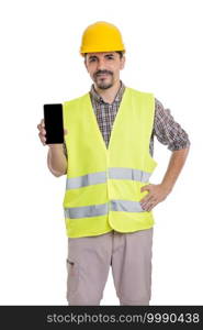Content male contractor wearing hardhat and yellow reflective vest standing with mobile phone on white background and looking at camera. Builder in uniform standing with smartphone on white background