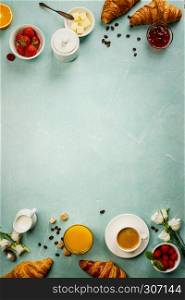 Continental breakfast captured from above top view, flat lay . Coffee, orange juice, croissants, jam, berry, milk and flowers. Blue concrete worktop as background. Layout with free text copy space.. Continental breakfast on blue background captured from above