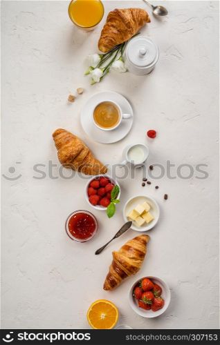 Continental breakfast captured from above top view, flat lay . Coffee, orange juice, croissants, jam, berry, milk and flowers. Grey stone worktop as background. Layout with free text copy space.. Continental breakfast captured from above, flat lay, top view