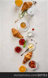 Continental breakfast captured from above top view, flat lay . Coffee, orange juice, croissants, jam, berry, milk and flowers. Grey stone worktop as background. Layout with free text copy space.. Continental breakfast captured from above, flat lay, top view