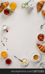 Continental breakfast captured from above top view, flat lay . Coffee, orange juice, croissants, jam, berry, milk and flowers. Grey stone worktop as background. Layout with free text copy space.. Continental breakfast captured from above - on concrete background