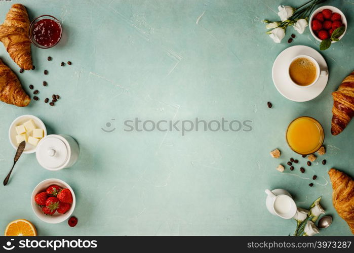 Continental breakfast captured from above top view, flat lay . Coffee, orange juice, croissants, jam, berry, milk and flowers. Blue concrete worktop as background. Layout with free text copy space.. Continental breakfast captured from above - space for text