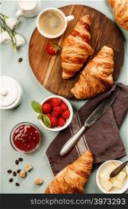 Continental breakfast captured from above top view, flat lay . Coffee, orange juice, croissants, jam, berry, milk and flowers. Blue concrete worktop as background. Layout with free text copy space.. Continental breakfast captured from above on concrete background