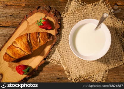 Continental breakfast with croissant, strawberries and a cup of milk seen from above