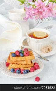Continental breakfast with sweet waffles, berries and tea with lemon