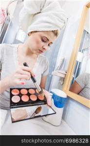 Contouring face kit, visage and make up concept. Woman in bathroom applying contour bronzer on brush. Woman in bathroom applying contour bronzer on brush