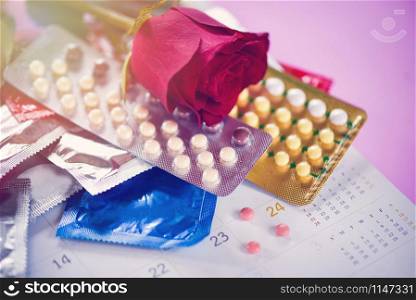 Contraceptive pill and Condom Prevent Pregnancy Contraception Valentines safe sex concept / Birth Control with Condom and roses on calendar background - pregnancy or sexually transmitted disease