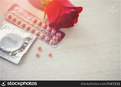 Contraceptive pill and Condom Prevent Pregnancy Contraception Valentines safe sex concept / Birth Control with Condom and roses on white wood background - pregnancy or sexually transmitted disease