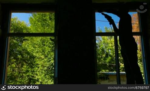 Contractor installing a new window in the house, bright trees and blue sky outside