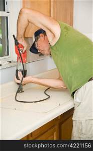 Contractor uses a reciprocating saw to cut through a formica counter top. Focus on saw.
