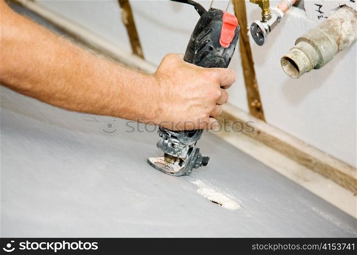 Contractor using a rotary saw to cut holes in drywall for the plumbing pipes. Authentic and accurate content depiction in accordance with industry safety and code standards.