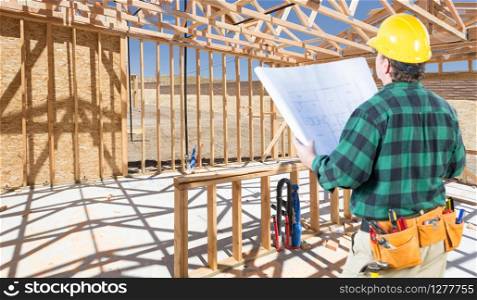 Contractor with hard Hat and Plans Standing Inside Construction Framing of New House.