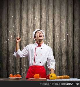 Cook at kitchen. Young cheerful cook and ingredients flying in air