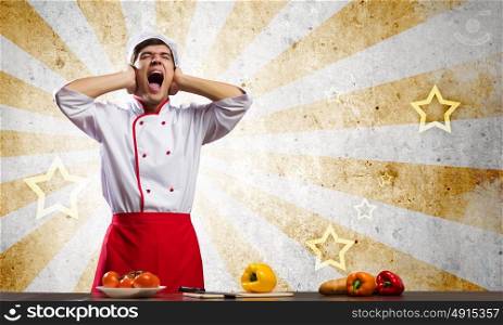 Cook at kitchen. Young screaming cook and vegetables on table