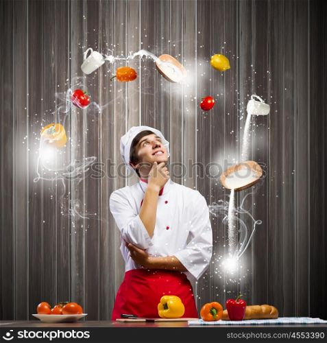 Cook at kitchen. Young thoughtful cook and ingredients flying in air