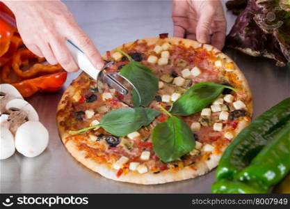 Cook cutting a Mediterranean pizza with vegetables and cheese