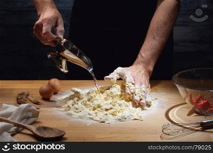 Cook hands kneading dough, adding water to flour. Low key shot, close up on hands, some ingredients around on table.