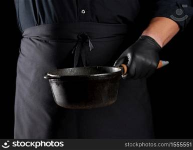 cook in black uniform and latex gloves holds an empty round vintage black cast iron pan in front of him, low key