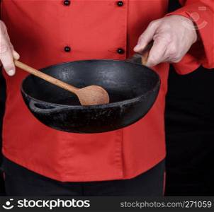 cook in red uniform holding an empty  black frying pan, black background