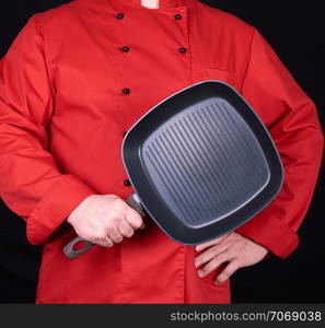 cook in red uniform holding an empty square black frying pan, black background