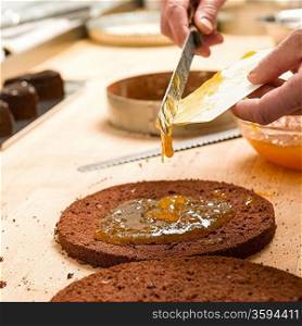 Cook making layer chocolate cake with orange marmalade