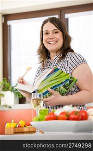 Cook - Plus size happy woman holding cookbook in kitchen