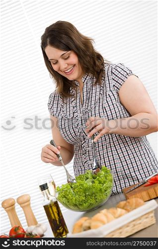 Cook - Plus size happy woman preparing vegetable salad with lettuce in modern kitchen
